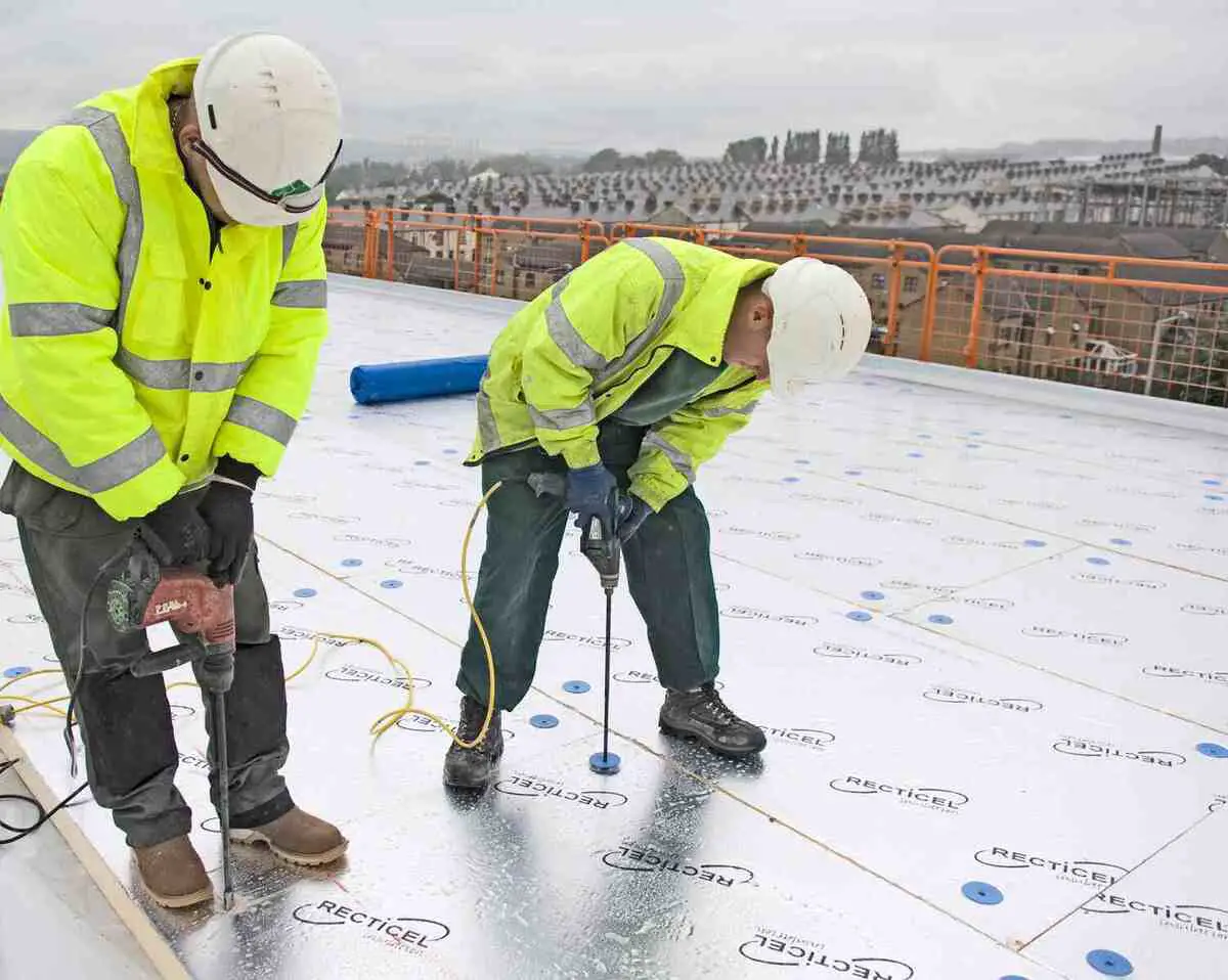 Workers installing a membrane roof system with safety gear